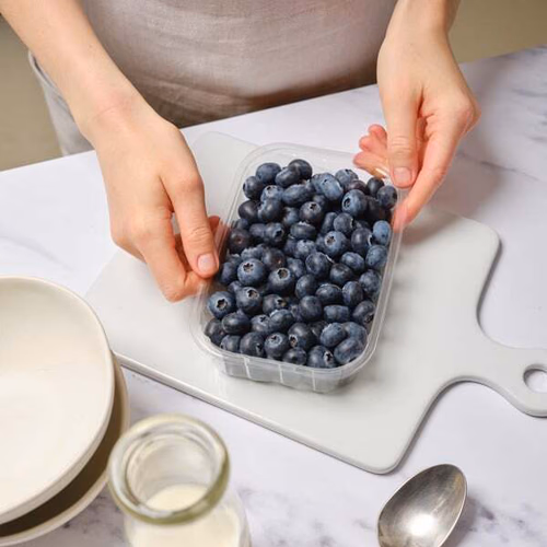 Blueberries in a punnet on a work surface held by a person out of frame