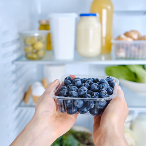Blueberry pack in hand in front of fridge